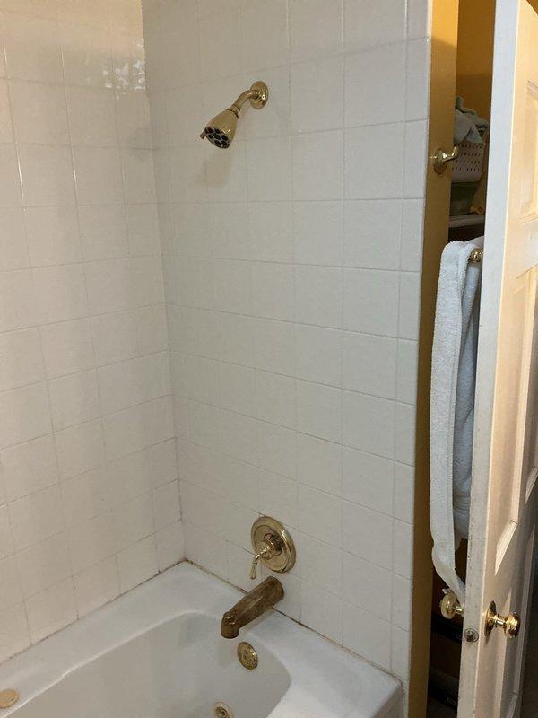Performed diagnostic inspection of bathroom to locate reported water leak. Inspected shower/tub installation, including brass fixtures, valve assembly, and drain connections. Assessed toilet for potential leakage and examined drainage system in bathtub that required rodding. Documented existing conditions with photographs showing aged brass fixtures and possible areas of water intrusion around tile grout and tub perimeter.