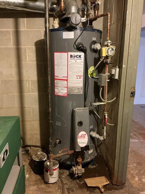 Conducted assessment of leaking water heater installation in basement utility room. Observed Bock brand unit with extensive copper piping system showing signs of corrosion and visible ceiling water damage near pipe connections. Estimate provided for complete replacement of existing water heater to address active leak and prevent further structural damage.