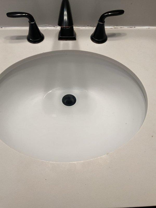 Responded to service call for bathroom sink reported clogged for approximately 2 weeks. Inspected white undermount oval basin with black drain and matte black fixtures. Examined P-trap assembly underneath consisting of black vertical drain pipe connected to white transitional piece and chrome P-trap. Successfully cleared blockage and verified proper drainage functionality.