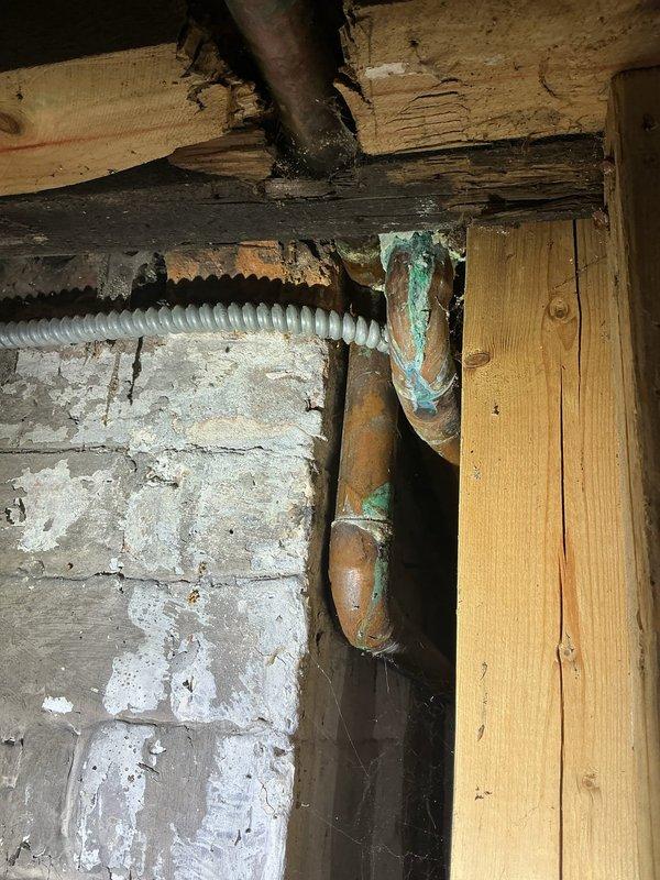 Conducted inspection of deteriorated drain stack in basement/crawlspace area. Observed significant corrosion on copper piping with visible green patina, particularly at joints and elbows. Identified potential water damage to surrounding wooden structural members where plumbing interfaces with building materials. Recommended replacement of cracked drain stack components to prevent further structural damage.