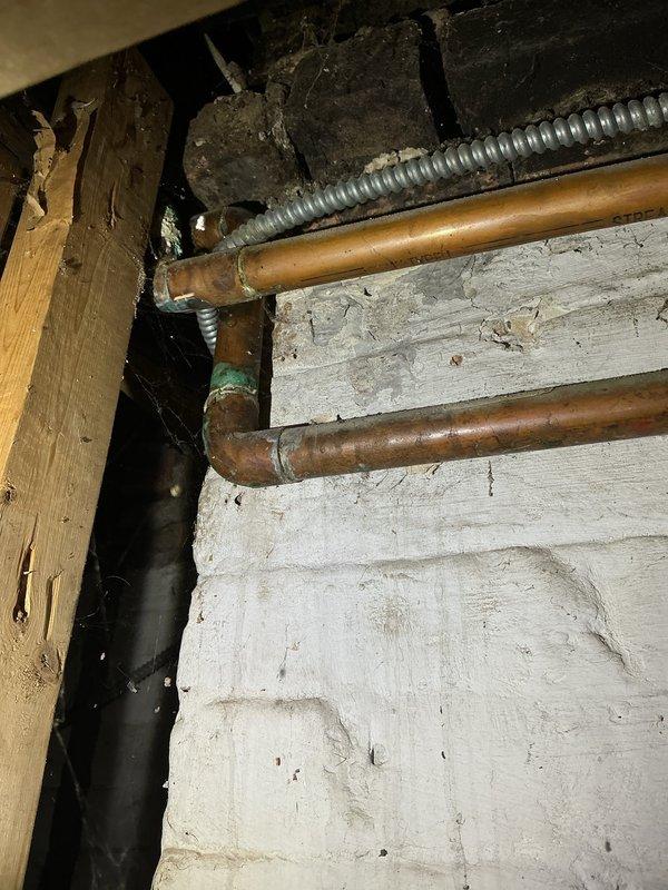 Conducted inspection of deteriorated drain stack in basement/crawlspace area. Observed significant corrosion on copper piping with visible green patina, particularly at joints and elbows. Identified potential water damage to surrounding wooden structural members where plumbing interfaces with building materials. Recommended replacement of cracked drain stack components to prevent further structural damage.