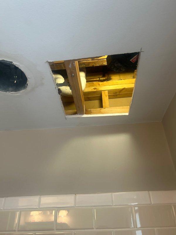 Responded to a reported ceiling leak in bathroom where water was dripping from a light fixture. Inspection revealed the source originated from plumbing in the ceiling of the bathroom above. Created access openings in the ceiling to expose the plumbing components, identifying brass pipes and connections requiring repair. Located and addressed the leak source to prevent further water damage.