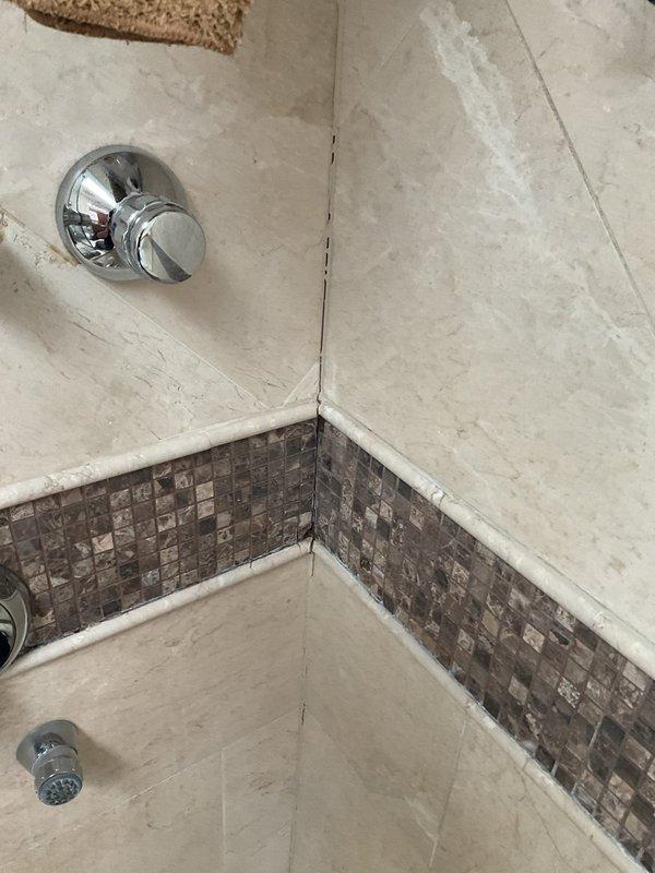 Investigated slow leak from kitchen ceiling originating from bathroom above. Inspection of the shower revealed aging grout and seam discoloration at tile joints, particularly in the corner where marble/stone tiles meet. Found potential moisture intrusion point near shower control valve and identified disconnected cable at stone shelf area that may relate to non-functioning steam shower system.