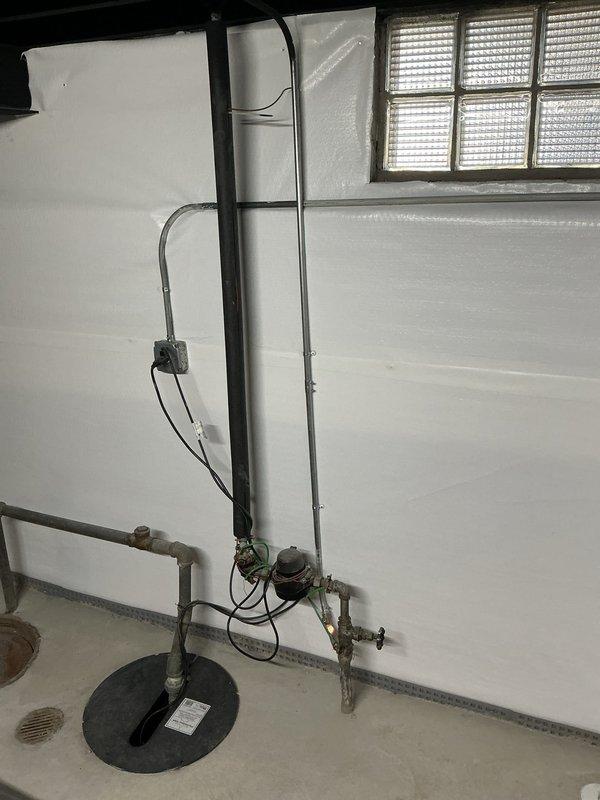 Conducted lead line replacement estimate in basement utility area. Inspected existing plumbing system including aging galvanized metal piping with visible tarnishing and minor corrosion, water meter with electrical connections, and sump pump installation. Documented current configuration with particular attention to L-shaped pipe arrangement with multiple joints and manual shut-off valves for replacement planning.
