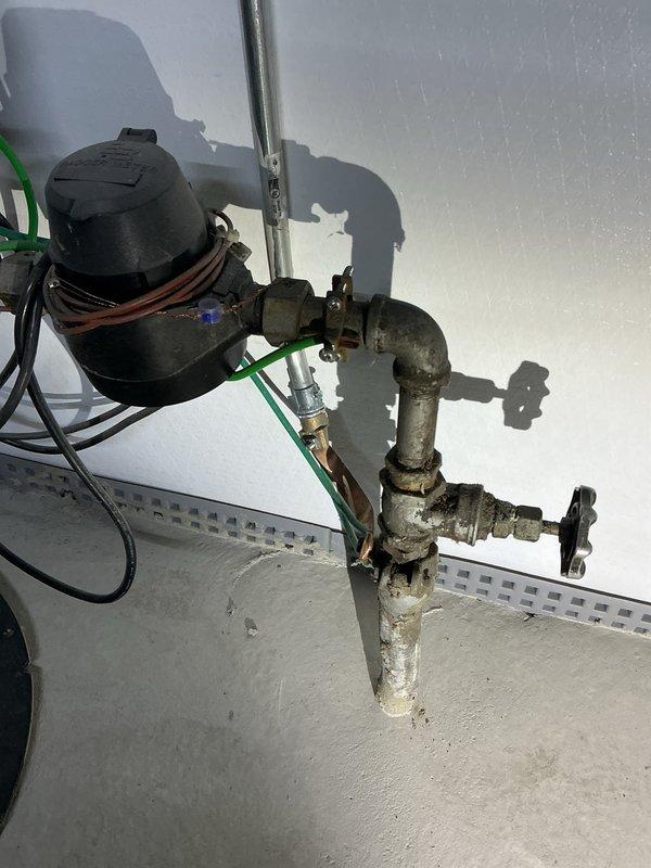 Conducted lead line replacement estimate in basement utility area. Inspected existing plumbing system including aging galvanized metal piping with visible tarnishing and minor corrosion, water meter with electrical connections, and sump pump installation. Documented current configuration with particular attention to L-shaped pipe arrangement with multiple joints and manual shut-off valves for replacement planning.