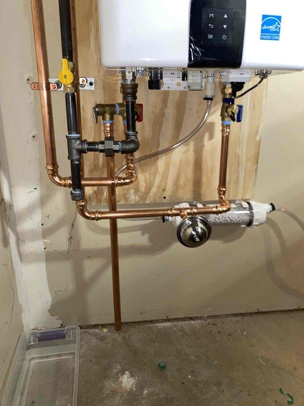 Installed new tankless water heater with complete copper pipe network and proper shut-off valves. Mounted unit securely on plywood backing board with appropriate venting system using PVC pipes and elbow joints. Installed condensation catch tray and tested all connections to ensure proper operation and energy efficiency.