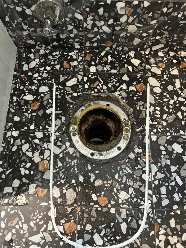 Responded to service call regarding toilet leaking onto floor in 70-year-old residence. Upon inspection, identified a corroded drain fixture in the terrazzo flooring as the source of the leak. Replaced broken steel component and verified proper operation of the toilet with no further leakage.