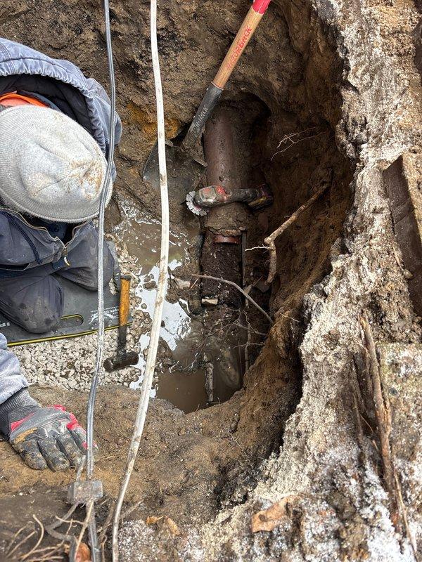 Conducted camera inspection of underground pipe system in excavated trench, documenting significant corrosion and deterioration of metal piping. Identified standing water accumulation at pipe connection point, likely indicating leak or drainage issue requiring repair. Visual examination revealed valve connection point with extensive rust damage requiring replacement.