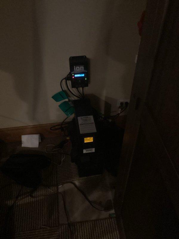 Installed Liberty PC backup sump pump system in basement, including dual PVC discharge lines with check valves and a wall-mounted electronic control unit with digital monitoring display. System features battery backup capability and was fully tested to ensure proper operation during power outages.