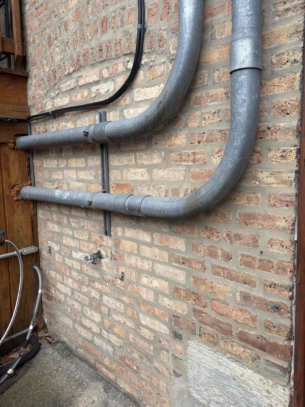 Conducted site assessment of existing plumbing infrastructure, including inspection of metal supply pipes mounted on brick wall with supporting brackets and examination of exterior PVC drainage stack with multiple joints and connections. Documented current installation conditions and prepared estimate for necessary piping modifications and repairs.