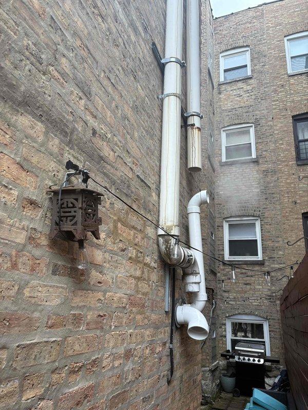 Conducted site assessment of existing plumbing infrastructure, including inspection of metal supply pipes mounted on brick wall with supporting brackets and examination of exterior PVC drainage stack with multiple joints and connections. Documented current installation conditions and prepared estimate for necessary piping modifications and repairs.