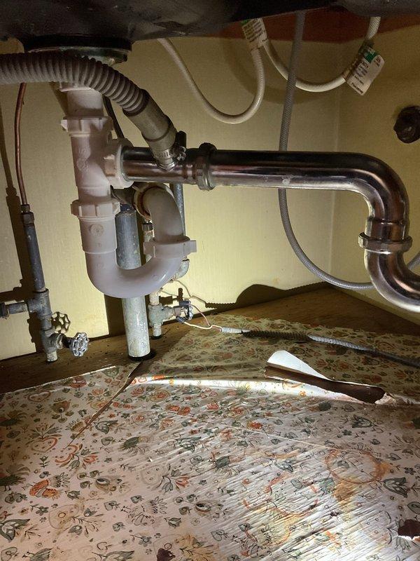 Responded to morning appointment for kitchen sink backup. Inspected P-trap configuration with both PVC and chrome pipes under sink, noting signs of water damage on the surrounding floor. Accessed wall panel to check drainage pathway, cleared blockage, and restored proper sink drainage function.