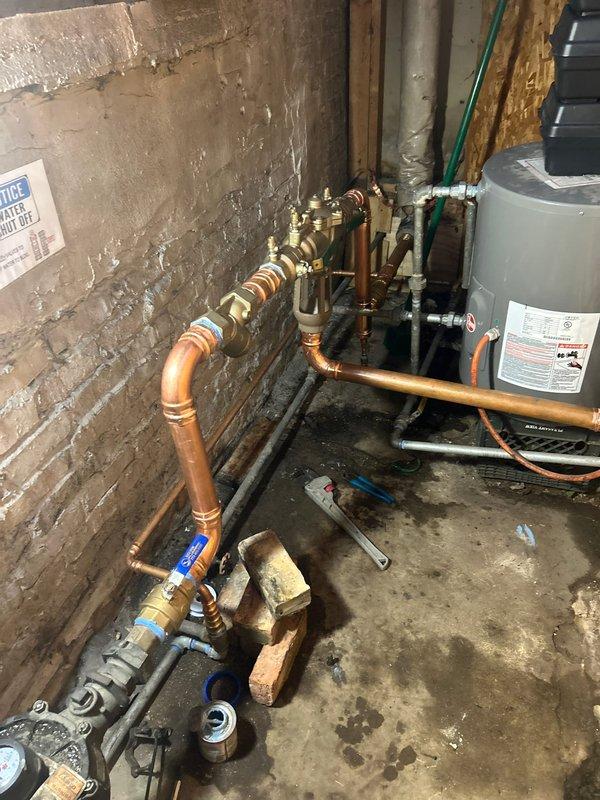 Installed copper piping for RPZ drain system in basement utility area, including necessary brass valves and fittings. Extended copper supply lines through bathroom, completing connections to existing plumbing infrastructure while maintaining proper support and alignment of all components.