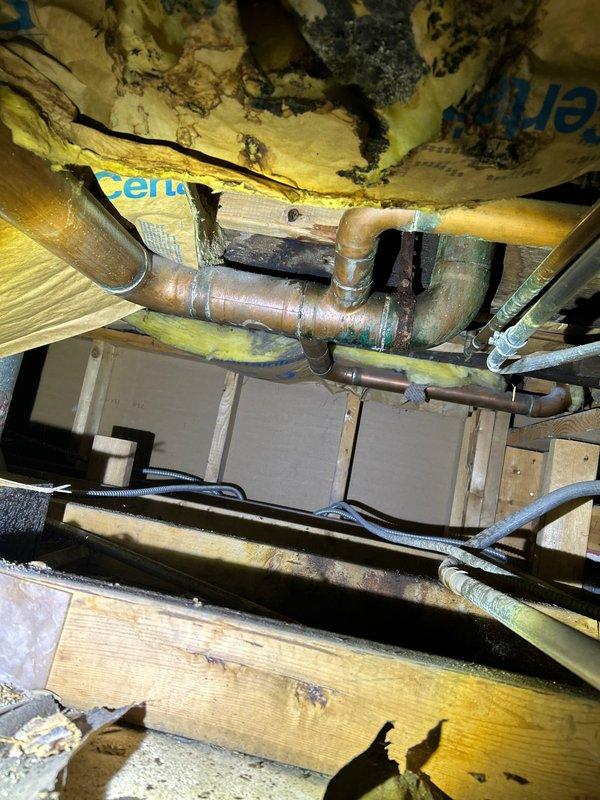 Investigated water leak from upstairs bathroom affecting master bathroom ceiling below. Inspection of exposed ceiling cavity revealed deteriorated insulation with black discoloration around copper plumbing pipes and compromised soldered joints at 90-degree connections. Repaired defective pipe joints, replaced damaged insulation, and verified system integrity with pressure testing.