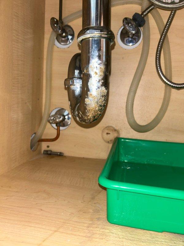 Diagnosed and repaired under-sink water leak originating from corroded chrome P-trap assembly with significant mineral buildup. Replaced damaged P-trap and inspected connected supply lines and brass fitting mounted on wall plate, ensuring proper connections and resolving the active leak that tenant had reported one day prior.