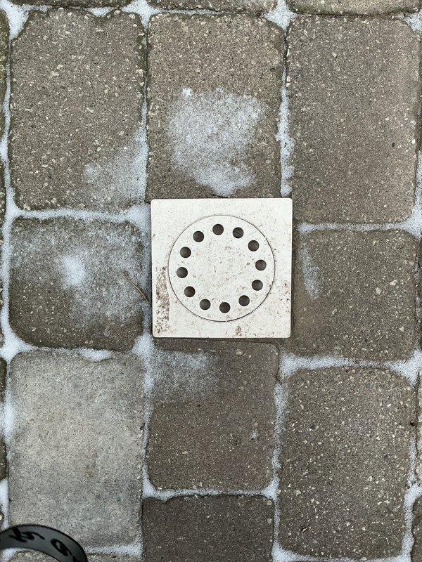 Conducted inspection of outdoor patio drainage system where water was slowly seeping through cracked drain. Documented square drainage cover embedded in stone pavers with visible deterioration around edges. No active backup was observed at time of assessment.