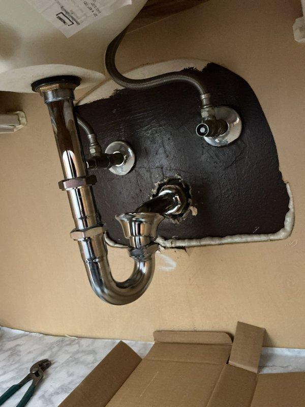 Repaired water leak under sink by replacing damaged P-trap assembly and drain connections. Installed new chrome P-trap with proper fittings and sealed pipe penetration in wall with caulking. Verified system integrity with no leaks after installation.