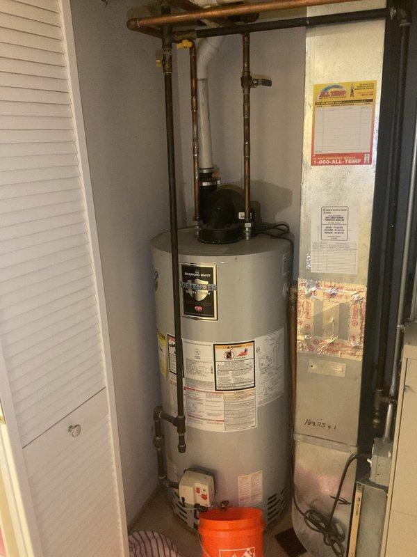 Inspected leaking tanked water heater in basement which showed visible cracking and water damage to surrounding concrete floor. Documented the existing installation including copper piping connections and gas valve assembly. Recommended complete replacement of the failed unit due to structural compromise and active leakage.