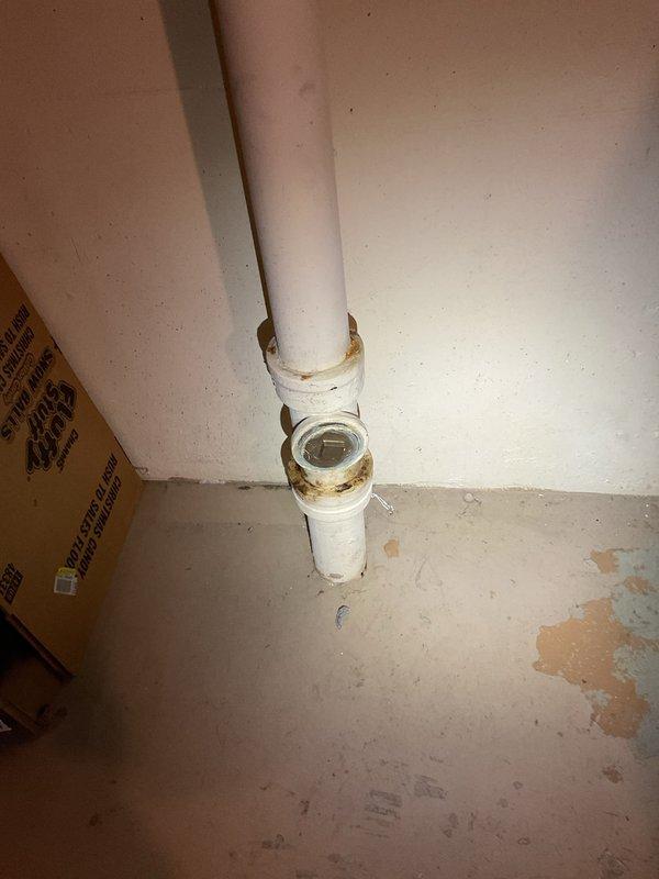 Responded to service call for suspected burst pipe under sink and main line rodding request. Inspected galvanized metal pipe showing signs of age and water damage to surrounding wooden surface. Serviced PVC plumbing installation with visible T-joint/cleanout fitting that showed discoloration and minor corrosion at connection points; cleaned and restored proper functionality to prevent further leakage.