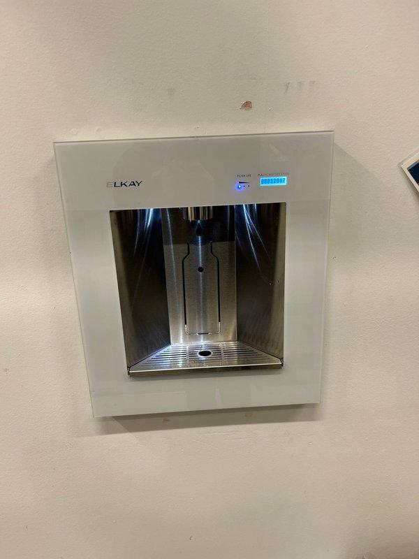 Replaced defective control board on Elkay water bottle filling station as per sold repair. Installed new circuit board in the control module housing, secured to stainless steel panel with mounting screws, and reconnected wiring harness. Unit now functioning properly with display showing correct bottle count and dispensing system operational.