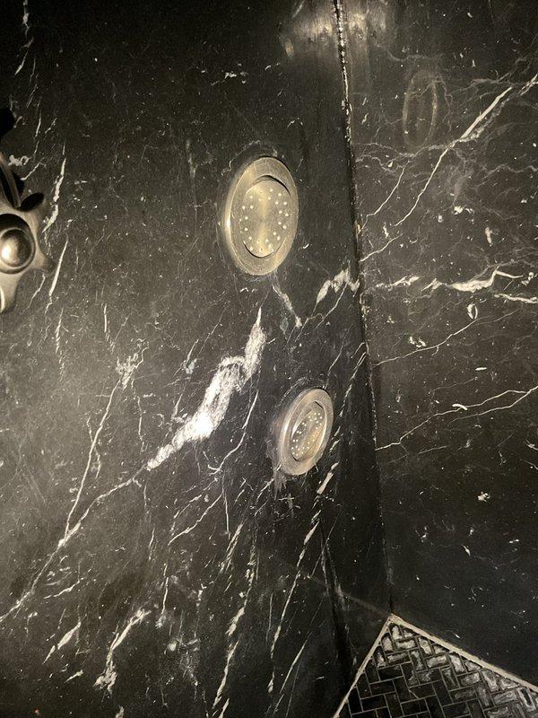 Responded to high water bill complaint in multi-unit building (9 condos, 1 commercial unit). Inspected decorative stone-mounted shower fixtures where two star-shaped control handles were installed in black marble. Identified water leak at fixture connection points with visible water marks on the stone surface, requiring adjustment of fittings to resolve the ongoing water loss issue.