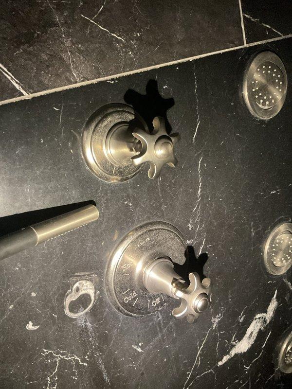 Responded to high water bill complaint in multi-unit building (9 condos, 1 commercial unit). Inspected decorative stone-mounted shower fixtures where two star-shaped control handles were installed in black marble. Identified water leak at fixture connection points with visible water marks on the stone surface, requiring adjustment of fittings to resolve the ongoing water loss issue.