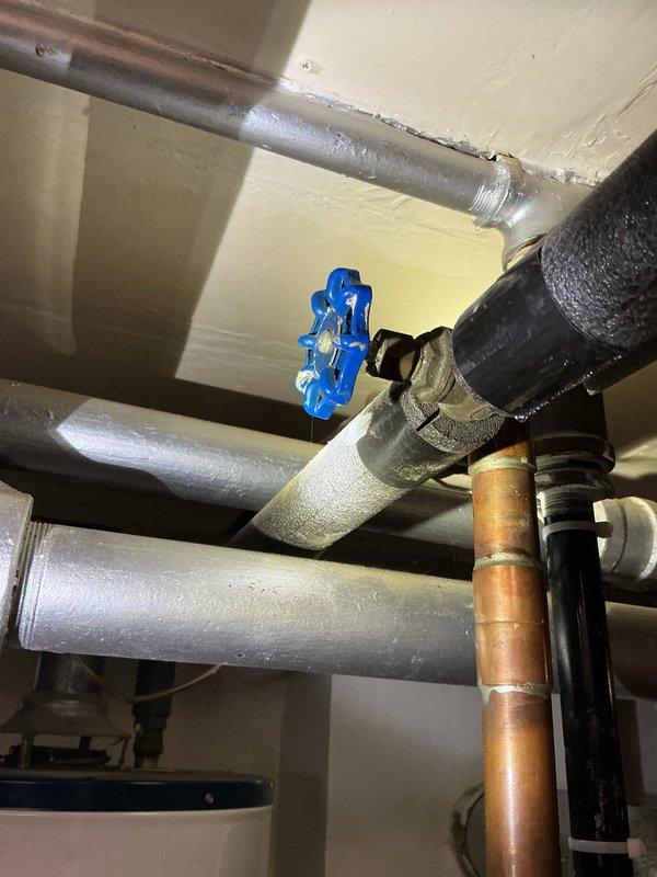 Conducted a comprehensive estimate for replacing an aging Whirlpool water heater installed in the utility room. Inspected the existing plumbing configuration, which includes a mix of galvanized steel, copper, and black pipes with multiple connection points and a prominent blue valve handle. Noted the current unit sits on a metal catch pan and would require coordination with the adjacent heating system components when performing the replacement.