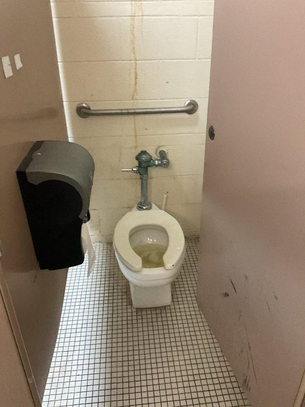 Conducted site assessment of commercial toilet installation in public restroom facility. Documented existing conditions including wall-mounted flush valve system, water staining on tile wall behind fixture, and overall condition of porcelain bowl and U-shaped seat. Provided customer with replacement options based on evaluation of current installation requirements.