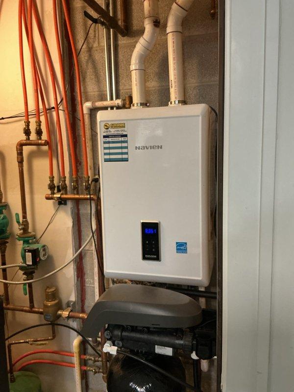 Successfully installed a Navien wall-mounted tankless water heater system with proper PVC venting and copper pipe connections. Unit was fully tested with all internal components verified for proper operation, including electronic control panels and circuit boards. Installation complete with all necessary valves and fittings against cinder block wall in utility area.