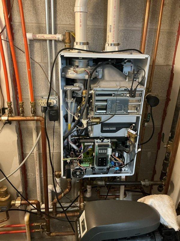 Successfully installed a Navien wall-mounted tankless water heater system with proper PVC venting and copper pipe connections. Unit was fully tested with all internal components verified for proper operation, including electronic control panels and circuit boards. Installation complete with all necessary valves and fittings against cinder block wall in utility area.