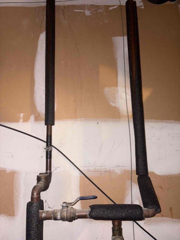 Responded to service call for low water pressure and pipe banging issues. Inspected plumbing system including insulated vertical pipes, copper lines, and pressure tank with attached pump. Diagnosed and adjusted the yellow flow control valve to restore proper water pressure and eliminate water hammer effect causing the sporadic banging noises.