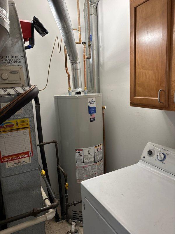 Inspected 16-year-old water heater that was leaking from the top connection points. Documented current installation in utility room with HVAC equipment and washing machine nearby. Recommended complete replacement due to age of unit and active leak.