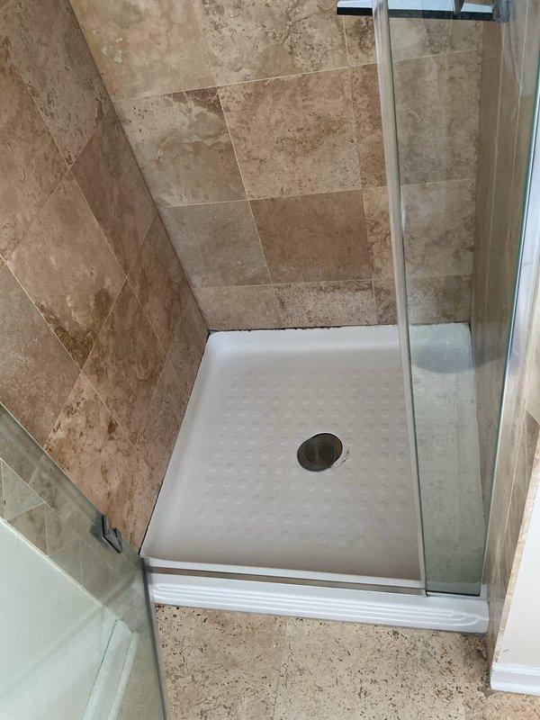 Conducted thorough inspection of shower stall with cracked shower pan and provided demolition quote for replacement. Documented existing installation including beige/tan tiled walls, white textured shower pan with circular drain, and glass door on chrome track for comprehensive repair estimate.