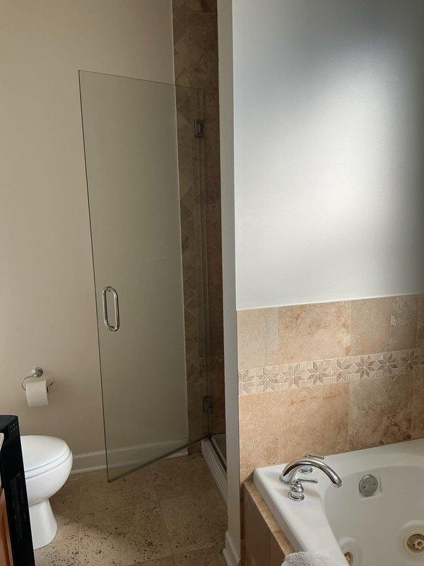 Conducted thorough inspection of shower stall with cracked shower pan and provided demolition quote for replacement. Documented existing installation including beige/tan tiled walls, white textured shower pan with circular drain, and glass door on chrome track for comprehensive repair estimate.