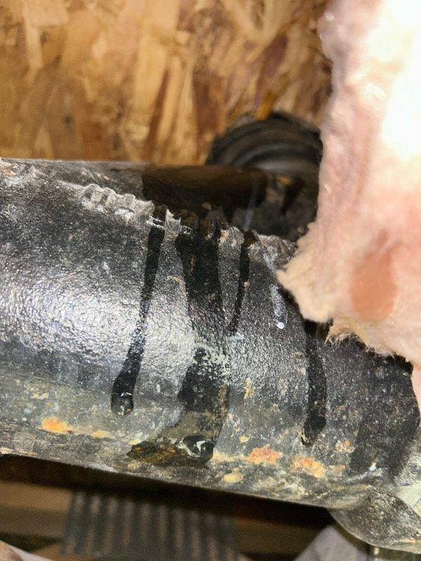 Conducted inspection of commercial ceiling area and identified significant leakage from a black metal pipe showing visible corrosion. Documented multiple streams of dark fluid dripping from the pipe surface with evidence of rust formation, potentially compromising the pipe integrity and ceiling structure. Recommended immediate replacement of affected piping sections to prevent further water damage to the surrounding OSB wall and insulation materials.