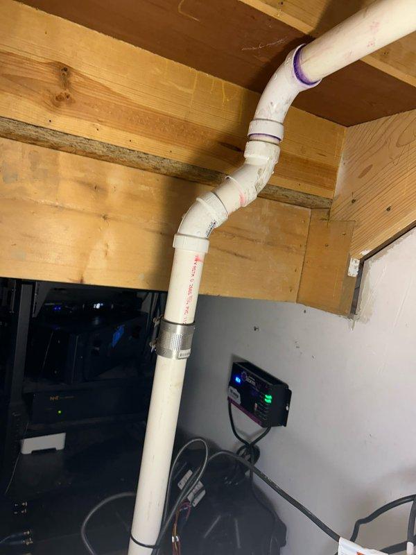 Conducted site assessment of basement sump pump system, documenting existing installation with black circular base plate showing corrosion and moisture issues. Evaluated current PVC discharge pipe configuration, noting S-shaped routing through floor joists with multiple elbow joints and connection points requiring attention. Scheduling immediate follow-up pending B-box discovery to implement proper waste pump solution.