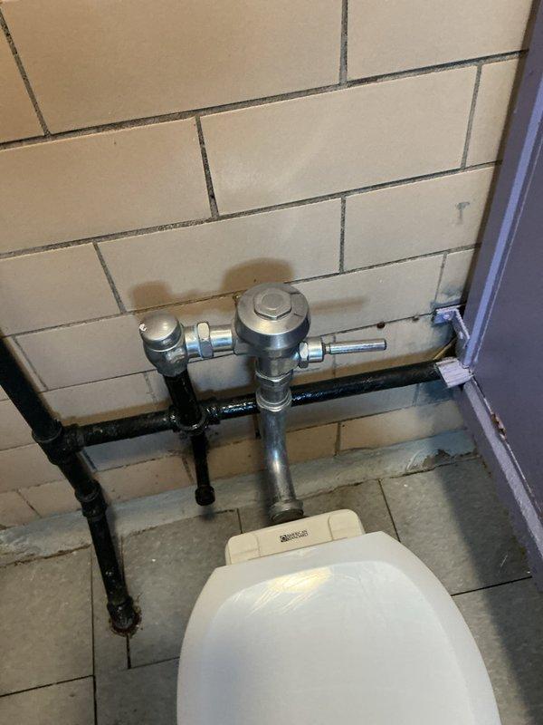Responded to service call back regarding commercial toilet installation. Inspected wall-mounted flush valve assembly showing signs of water staining on surrounding tiles. Serviced the chrome flushometer valve system and checked all connecting pipes for proper function and installation integrity.