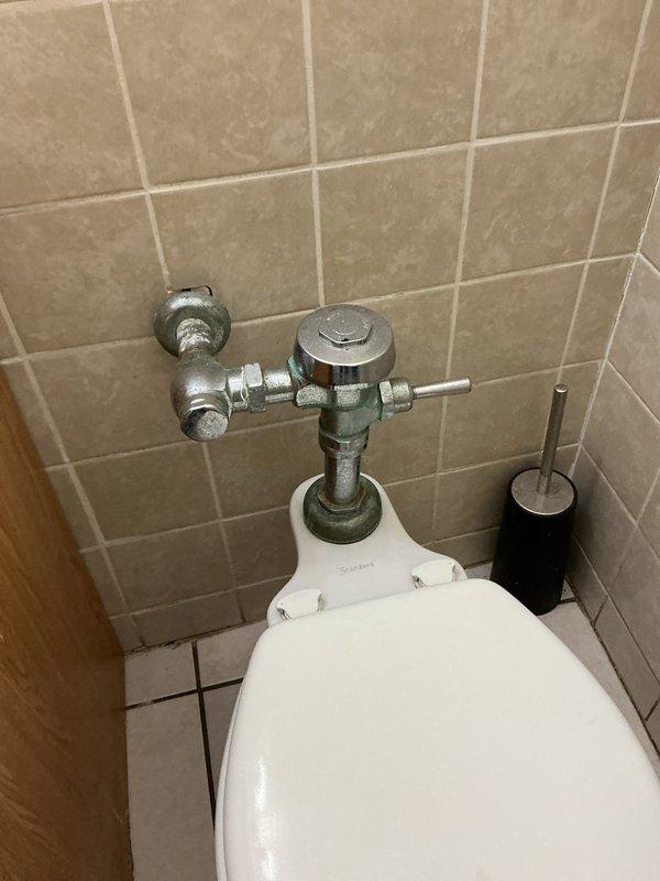 Responded to service call back regarding commercial toilet installation. Inspected wall-mounted flush valve assembly showing signs of water staining on surrounding tiles. Serviced the chrome flushometer valve system and checked all connecting pipes for proper function and installation integrity.
