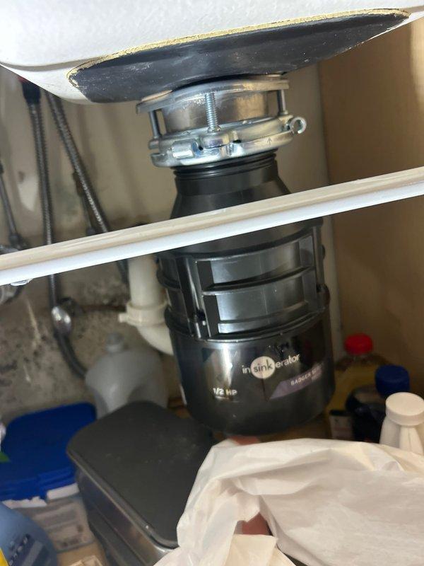 Responded to reported kitchen sink leak in condo unit with unknown duration. Inspection revealed InSinkErator 1/2 HP garbage disposal with visible corrosion and mineral buildup at the mounting assembly. Replaced deteriorated disposal mounting gasket and tightened loose connections to resolve the leak.