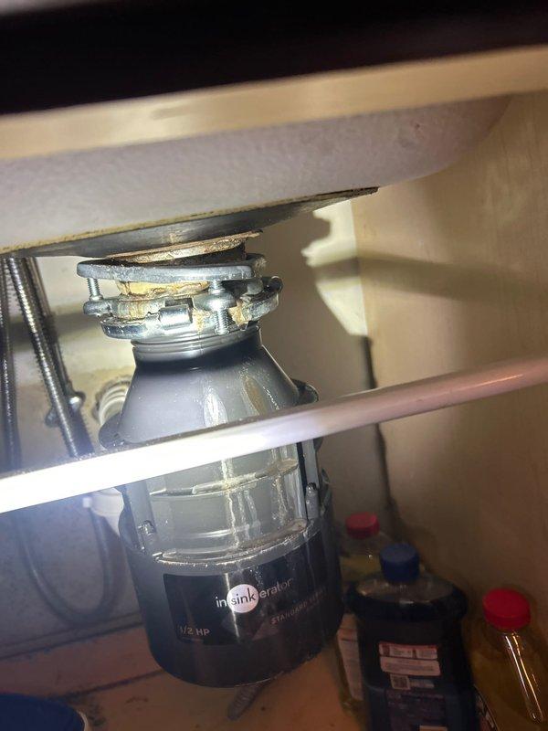 Responded to reported kitchen sink leak in condo unit with unknown duration. Inspection revealed InSinkErator 1/2 HP garbage disposal with visible corrosion and mineral buildup at the mounting assembly. Replaced deteriorated disposal mounting gasket and tightened loose connections to resolve the leak.