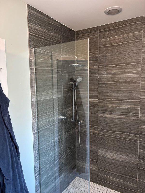 Responded to service call regarding foul odor emanating from shower drain. Conducted thorough inspection of the modern walk-in shower with horizontal striped tile walls and glass door panel. Located and cleared clogged P-trap containing organic debris buildup, which was causing the reported smell. After cleaning, performed flow test to confirm proper drainage and ventilation.
