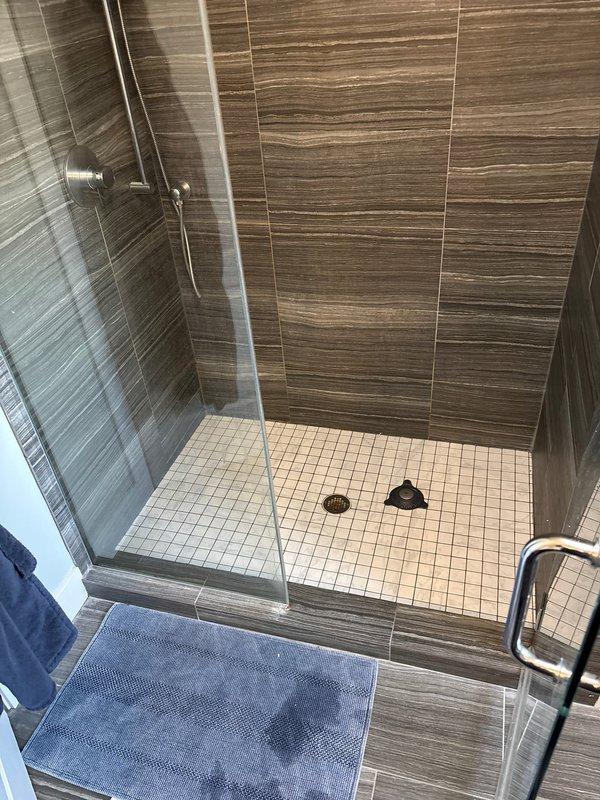 Responded to service call regarding foul odor emanating from shower drain. Conducted thorough inspection of the modern walk-in shower with horizontal striped tile walls and glass door panel. Located and cleared clogged P-trap containing organic debris buildup, which was causing the reported smell. After cleaning, performed flow test to confirm proper drainage and ventilation.