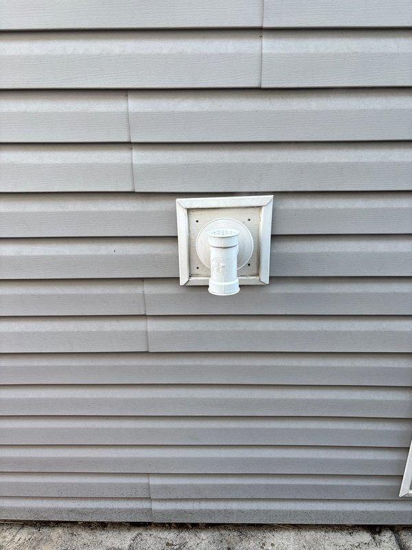 Completed installation of exterior vent for client's home ventilation system. Mounted white plastic vent fixture with square base plate and circular center to exterior light gray vinyl siding, ensuring proper sealing and secure attachment. Job originally sold by Jon.
