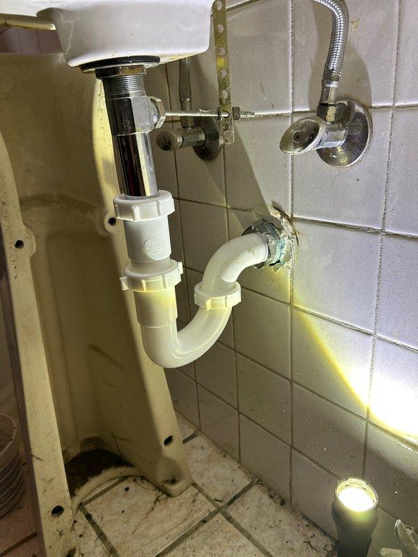 Located and identified source of bathroom sink leak as severely deteriorated drain pipe with significant corrosion and mineral buildup. Documented active water leakage from the bottom of the P-trap assembly, which showed multiple areas of deterioration including yellowish-brown deposits at the fixture connection point and extensive oxidation throughout the curved section.