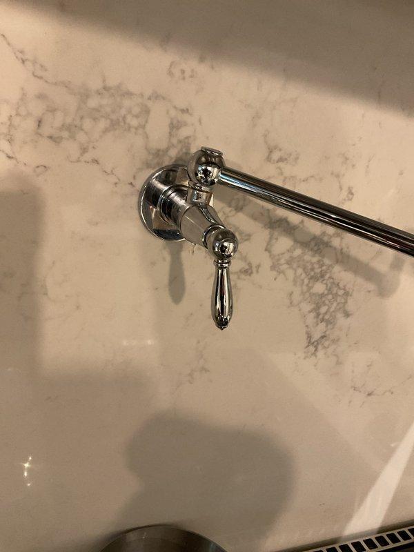 Successfully replaced broken bathroom faucet with a new chrome model featuring angular design and separate handle components, installing it properly on the light beige countertop with the decorative herringbone backsplash. Also inspected and repaired kitchen faucet drip issue located above stove.