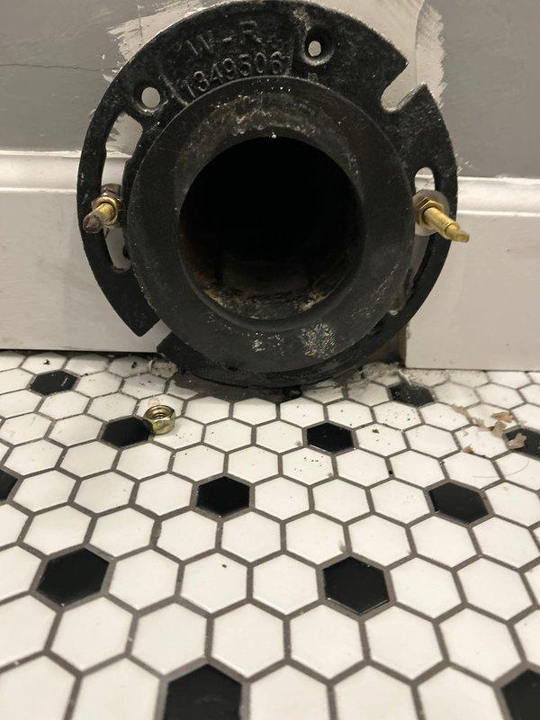 Successfully installed a toilet by properly connecting it to an existing cast iron flange on hexagonal tile flooring. Secured the toilet using the brass mounting bolts already in place on the flange, ensuring a proper seal and stable fixture installation. Verified proper installation with photos showing the ML-R 1340506 flange before final toilet placement.