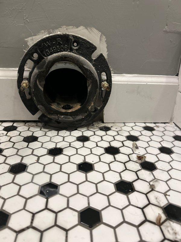 Successfully installed a toilet by properly connecting it to an existing cast iron flange on hexagonal tile flooring. Secured the toilet using the brass mounting bolts already in place on the flange, ensuring a proper seal and stable fixture installation. Verified proper installation with photos showing the ML-R 1340506 flange before final toilet placement.