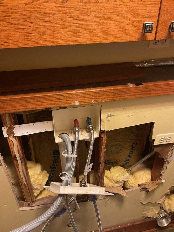 Performed commercial estimate for plumbing repairs beneath sink fixture with significant wall damage. Inspection revealed deteriorated drywall around hot and cold water supply lines, exposed fiberglass insulation between wall studs, and compromised plumbing connection box. Documented extensive water damage requiring remediation and potential cabinet/wall reconstruction.