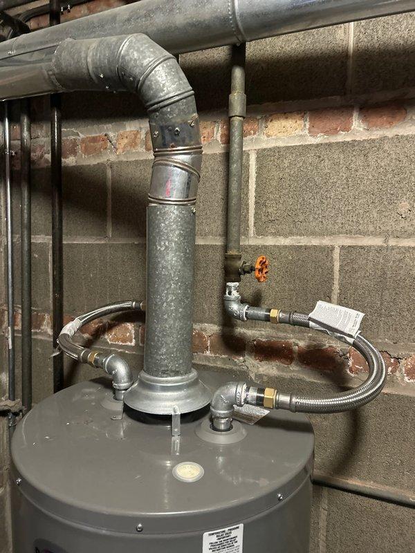Completed galvanized pipe repair on water line connected to tanked water heater. Installed new metal flexible connector lines with brass fittings and secured proper connections to existing plumbing system. Verified integrity of exhaust ventilation system with 90-degree elbow joint connecting to horizontal vent pipe, ensuring installation meets code requirements.