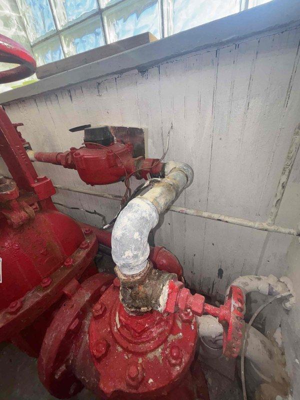 Performed site visit to assess water service issue where occupants had no water supply and were unable to use facilities. Inspection revealed significant corrosion and mineral buildup at connection points between the red painted pipes and PVC components of the water system. Documented extensive deterioration at pipe joints with visible rust and water damage to surrounding wall areas; determined city needs to replace shut-off at meter vault before further repairs can proceed.